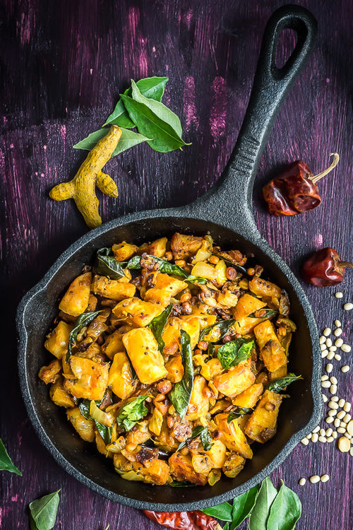 Spicy dish in a black skillet on a dark background with spices and herbs.