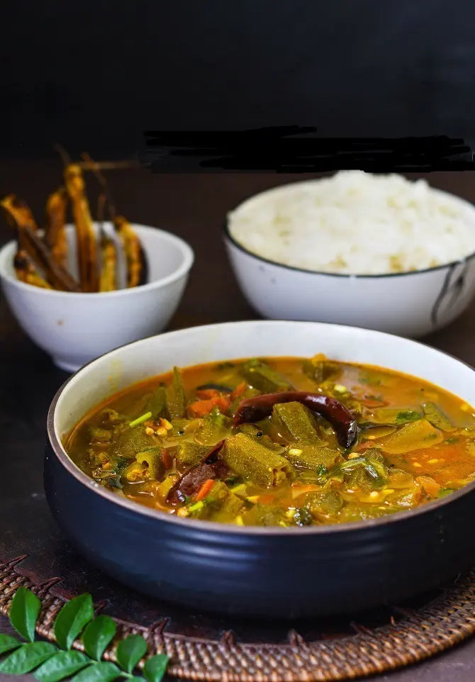 Bowl of curry with a side of rice and pickles on a dark background